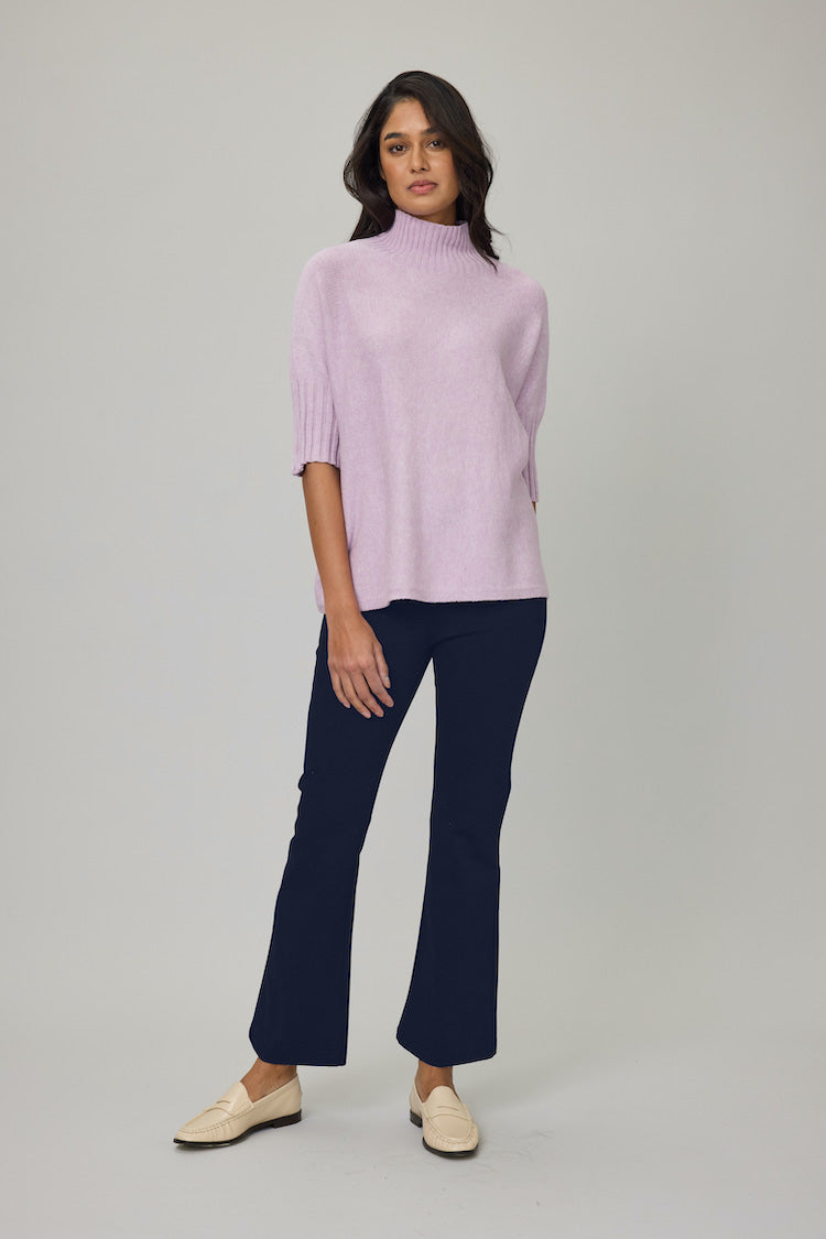 Woman wearing a light purple turtleneck and dark blue flared pants on a gray background