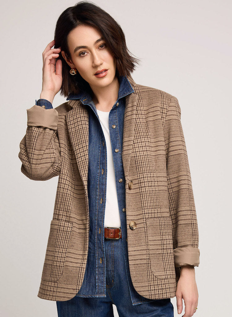Woman wearing a brown checkered jacket over a denim shirt and jeans on a plain background