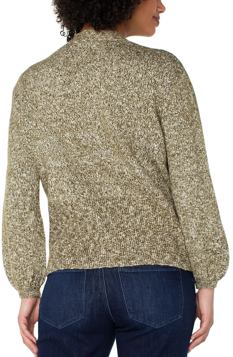 Woman wearing a patterned sweater and dark jeans on a white background