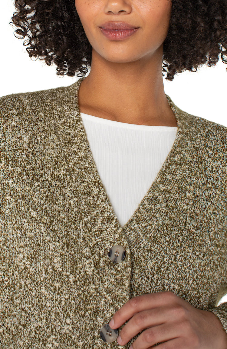 Person wearing a textured cardigan over a white shirt with a neutral background