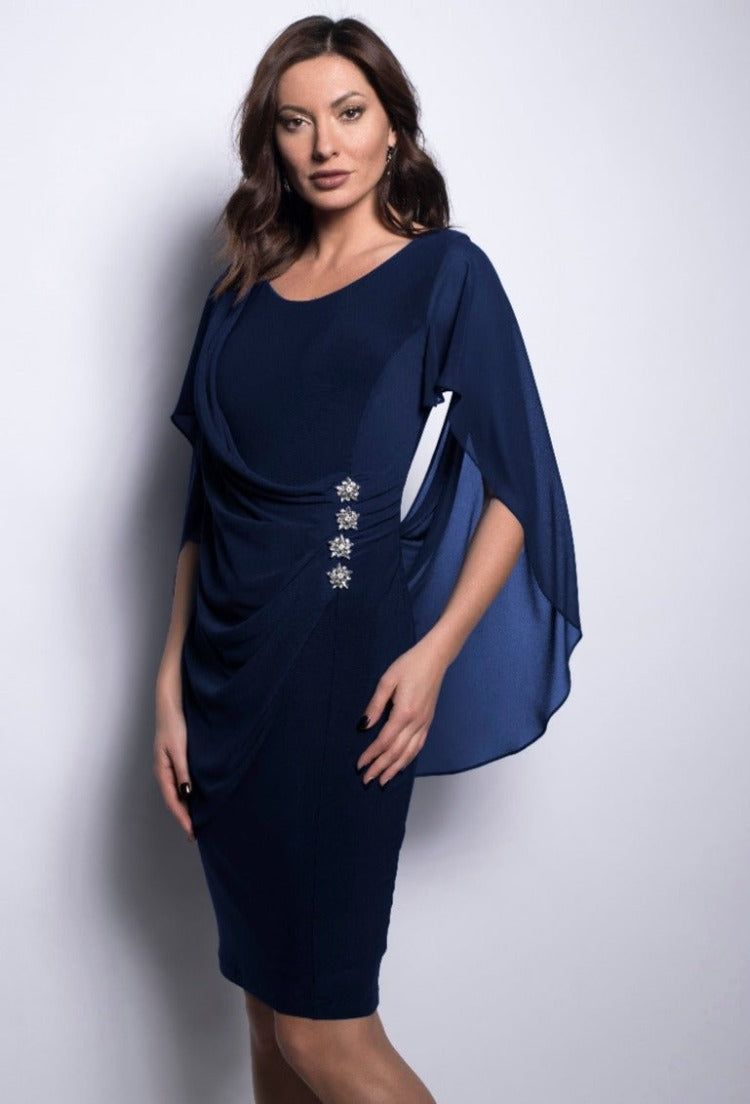 Make an unforgettable entrance at your next event with this Cape Jewel Dress from Frank Lyman. This showstopper features a gorgeous cape-style overlay that drapes over your shoulders and flattering ruching fastened by four jeweled flowers in the front. Made in Canada.