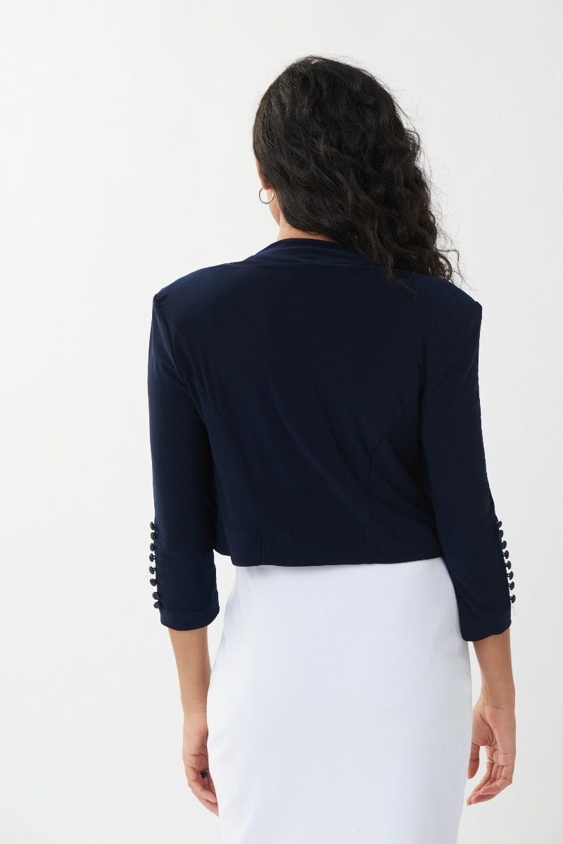 A favorite piece for any wardrobe.  Joseph Ribkoff Bolero Style Top is a lovely cover up.   It features an open front, cropped cut with bold, clean lines, three quarter length sleeves with button detail accents at the elbow.  Beautifully fitted shoulders with shoulder pads for a classically elegant yet modern look.  