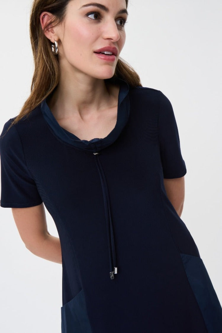 With its fun contrasting materials give this fabulous Joseph Ribkoff Cowl Neck Drawstring Dress   a sporty look. Having front patch pockets and a drawstring in the neck is what gives this A-line dress it's athletic style. You will have the best of comfort and style every time you wear it.
